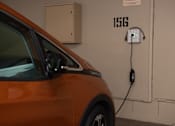 Thumbnail 51 of 57 - An orange car is plugged into a charging station labeled 156.
