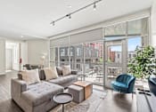 Thumbnail 67 of 131 - A modern living room with a grey sofa and a glass door leading to a balcony.