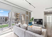 Thumbnail 69 of 131 - A living room with a grey couch and a balcony with a view of the city.