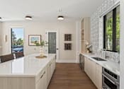 Thumbnail 6 of 46 - A modern kitchen with a white countertop and wooden cabinets.