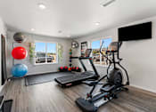 Thumbnail 47 of 74 - a gym with exercise equipment and a tv on the wall at Red Rock Apartments, South Dakota