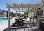 Thumbnail 11 of 35 - a patio with a grill and a table with chairs and a pool at City View St. George Apartments, St George, UT, 84770