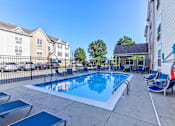 Thumbnail 20 of 45 - A swimming pool with lounge chairs and umbrellas is surrounded by apartment buildings.