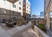 Thumbnail 15 of 84 - a patio with benches and tables in front of an apartment building at The Revival, Utah
