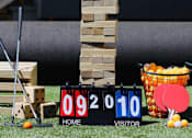 Thumbnail 40 of 45 - A game of Jenga is set up on a lawn with a scoreboard and ping pong paddles and balls nearby.