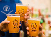 Thumbnail 37 of 45 - A person holding three cups of Union beer.
