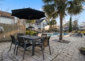 Thumbnail 40 of 61 - a patio with a table and chairs under an umbrella next to a pool at AVIA Lofts on Liberty Ridge, Florida