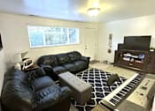 Thumbnail 3 of 14 - A black leather couch sits in a living room with a piano in the corner.