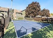 Thumbnail 32 of 92 - A tennis court surrounded by a fence and trees.