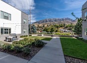 Thumbnail 5 of 136 - a sidewalk in front of a building with a table and chairs on it at The Flats at Riverwoods, Provo, Utah