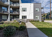 Thumbnail 4 of 136 - an exterior view of an apartment building with a sidewalk and grass at The Flats at Riverwoods, Provo, Utah