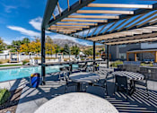 Thumbnail 97 of 136 - a patio with tables and chairs next to a pool at The Flats at Riverwoods, Provo, Utah