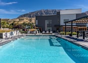 Thumbnail 93 of 136 - a swimming pool with a building and mountains in the background at The Flats at Riverwoods, Provo