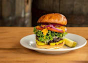 Thumbnail 39 of 45 - A burger with lettuce, tomato, pickles, and onions is on a plate.