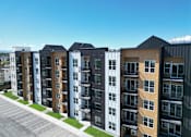 Thumbnail 49 of 144 - A row of modern apartment buildings with a parking lot in front.
