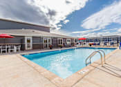 Thumbnail 29 of 74 - A pool with a red umbrella and a building in the background. at Red Rock Apartments, Rapid City, 57702