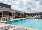 Thumbnail 32 of 74 - a swimming pool with lounge chairs and tables and a building in the background at Red Rock Apartments, Rapid City, South Dakota