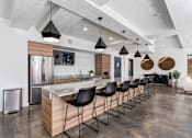 Thumbnail 21 of 136 - a kitchen with a long island with black chairs and a stainless steel refrigerator at The Flats at Riverwoods, Provo