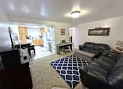 Thumbnail 1 of 14 - A living room with a black leather couch and a rug.