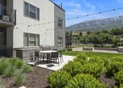 Thumbnail 6 of 136 - a patio with a table and chairs in front of a building at The Flats at Riverwoods, Provo