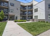 Thumbnail 8 of 136 - a view of the back of the building with a lawn and patio at The Flats at Riverwoods, Provo, UT