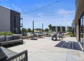 Thumbnail 19 of 136 - a patio with couches and chairs and string lights in front of a building at The Flats at Riverwoods, Utah