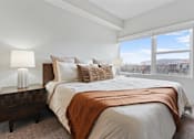 Thumbnail 20 of 71 - A bedroom with a large bed and a window overlooking a cityscape at Wilmington Flats Apartments, Salt Lake City