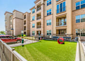 Thumbnail 9 of 27 - A red car is parked in front of a building with a green lawn and a red sculpture at Atlas Point at Prestonwood Apartments , Carrollton, TX