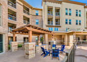 Thumbnail 2 of 27 - A patio with a table and chairs is surrounded by apartment buildings. at Atlas Point at Prestonwood Apartments , Carrollton, TX