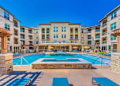 Thumbnail 1 of 27 - A large swimming pool in front of a multi-story apartment building. at Atlas Point at Prestonwood Apartments , Carrollton, Texas