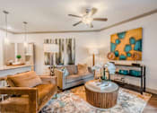 Thumbnail 21 of 27 - A living room with a brown leather chair, a grey sofa, a wooden coffee table, and a painting on the wall at Atlas Point at Prestonwood Apartments , Carrollton