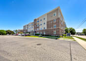 Thumbnail 5 of 28 - A large parking lot in front of a multi-story apartment building.