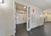 Thumbnail 18 of 28 - A hallway with doors and a fire alarm on the wall.