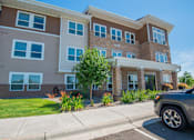 Thumbnail 6 of 8 - A modern two-story apartment building with a car parked in front.
