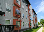 Thumbnail 5 of 12 - A tree with red leaves is in front of a grey building with orange trim.