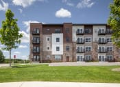 Thumbnail 6 of 52 - an apartment building with brick and stone exterior and green grass