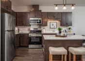Thumbnail 2 of 19 - A modern kitchen with a refrigerator, oven, and bar stools.