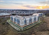 Thumbnail 20 of 20 - A large apartment complex is surrounded by a grassy area and a wall.