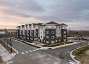 Thumbnail 1 of 11 - A large apartment complex with a parking lot in front.