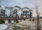 Thumbnail 7 of 11 - A large, modern apartment complex with a mix of grey and beige exterior walls.