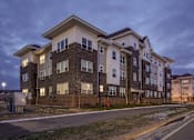 Thumbnail 11 of 11 - A large apartment building with multiple balconies and windows is shown at dusk.