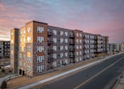 Thumbnail 7 of 24 - A large apartment building with a parking lot in front.