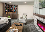 Thumbnail 14 of 24 - A living room with a black couch, a chair, a coffee table, and a bookshelf.