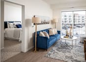 Thumbnail 5 of 24 - A blue couch with a gold floor lamp and a white table with a vase on it.