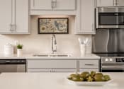 Thumbnail 6 of 24 - A modern kitchen with a stainless steel oven and a framed picture on the wall.