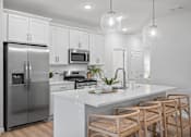 Thumbnail 8 of 15 - A modern kitchen with a stainless steel refrigerator, white cabinets, and wooden chairs.