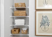 Thumbnail 31 of 62 - A bathroom with a white wall and a shelf with baskets and towels.