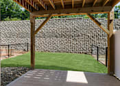 Thumbnail 47 of 62 - A wooden pergola over a concrete patio with a stone wall in the background.