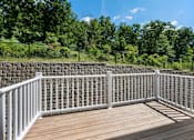Thumbnail 50 of 62 - A white railing on a wooden deck with a stone wall and trees in the background.
