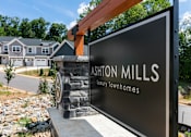 Thumbnail 60 of 62 - A sign for Ashon Mills Luxury Townhomes stands in front of a house.